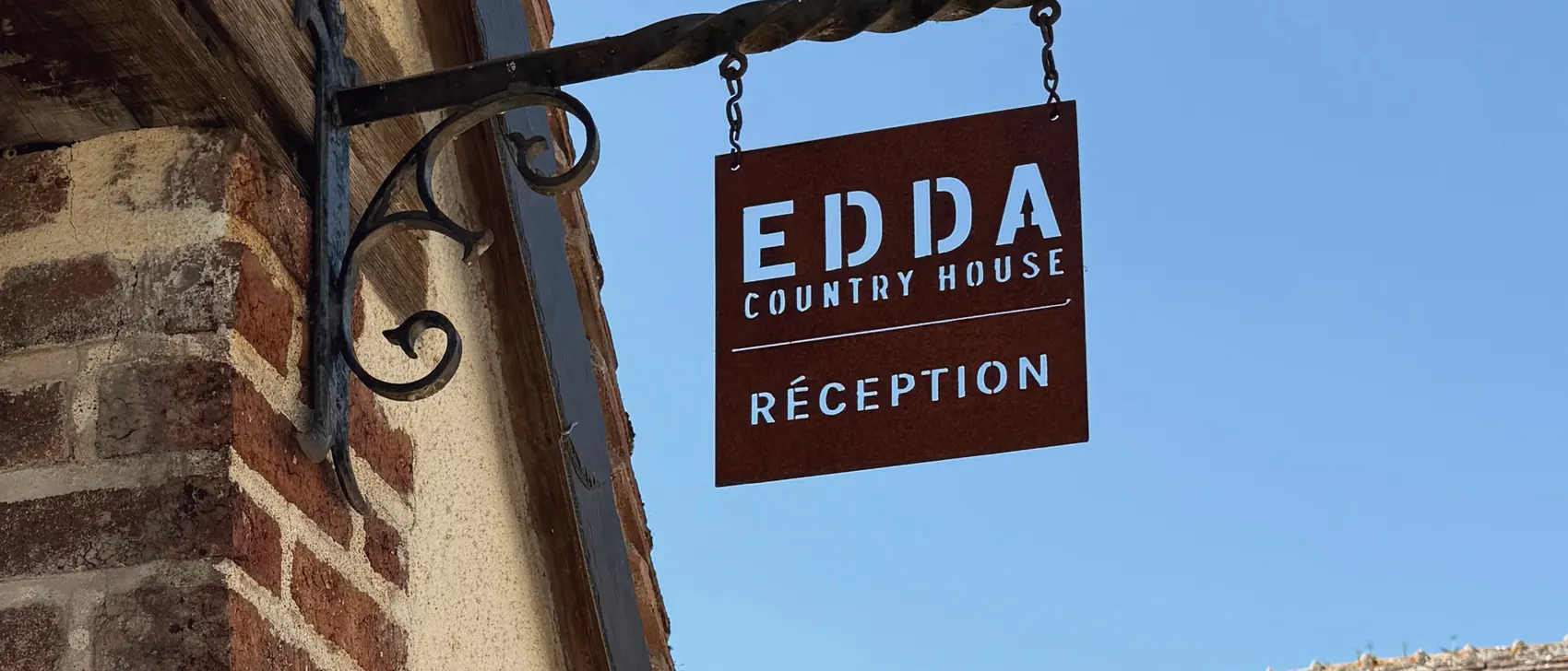 L'enseigne EDDA Country House en fer forgé, contre le mur de brique de la maison