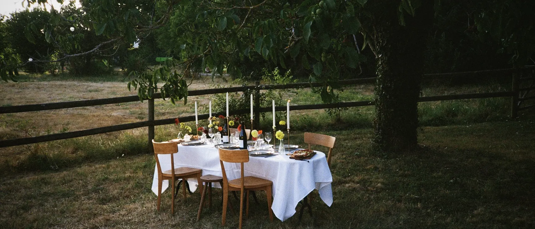 Une table dressée sous les arbres du jardin, à la tombée du jour